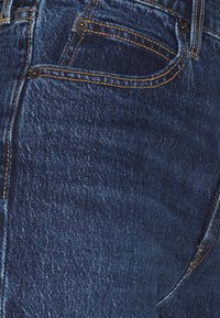 Džíny z denimu v tmavě modré barvě s mírnou elasticitou. Mají měděné prošívání, přední kapsy a kovové nýty. Texturovaný vzor na povrchu.