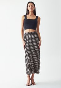 Čierny crop top so štvorcovým výstrihom skombinovaný s dlhou vzorovanou sukňou v čiernej a krémovej farbe s opakujúcimi sa kvetinovými motívmi. Popruhové čierne podpätky.