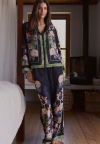 Set di pigiama in seta floreale con sfondo nero e accenti verdi, grandi motivi di fiori e un fit rilassato. Maglia con bottoni e pantaloni ampi.