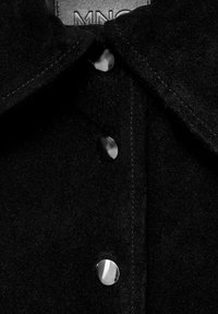 Camicia in suede nero con colletto a punta e bottoni a pressione metallici. La texture morbida e la finitura lucida mettono in risalto le caratteristiche di design del capo.