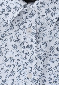 Chemise blanche à col avec un motif abstrait de feuilles bleues et des boutons blancs le long de la patte de boutonnage avant.