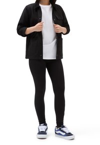 Giacca nera a bottone sopra una maglietta bianca, abbinata a leggings neri e sneakers blu navy. La giacca ha due tasche frontali e maniche arrotolate.