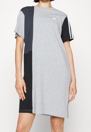 Mujer con vestido Adidas de manga corta y largo hasta la rodilla, con bloques de color gris y negro y rayas blancas en una manga.