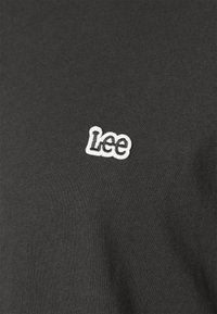 Schwarzes Baumwoll-T-Shirt mit einem weißen, gestickten "Lee"-Logo auf der linken Brust. Der Stoff hat eine glatte, strukturierte Oberfläche.