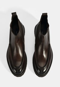 Bottes en cuir marron de cheville avec des côtés en élastique, des bouts ronds et un détail texturé contrasté le long des coutures. Fini mat.