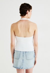 Top alb cu bretele din material elastic, asortat cu o fustă mini din denim de culoare albastră deschisă, având două buzunare la spate. Textură netedă și design ajustat.