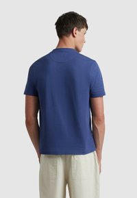 T-shirt a maniche corte concollo tondo in tessuto blu uniforme, caratterizzato da un design semplice e una superficie liscia. Indossato con pantaloni di colore chiaro.