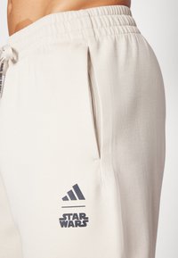 Beiga sweatpants i mjukt material med elastisk midja. Har sidofickor och svarta Adidas- och Star Wars-logotyper på låret.