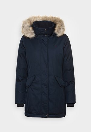 Parka d’hiver bleu marine avec bordure de capuche en fausse fourrure, poches à rabat à l’avant, col montant et fermeture par boutons cachés.