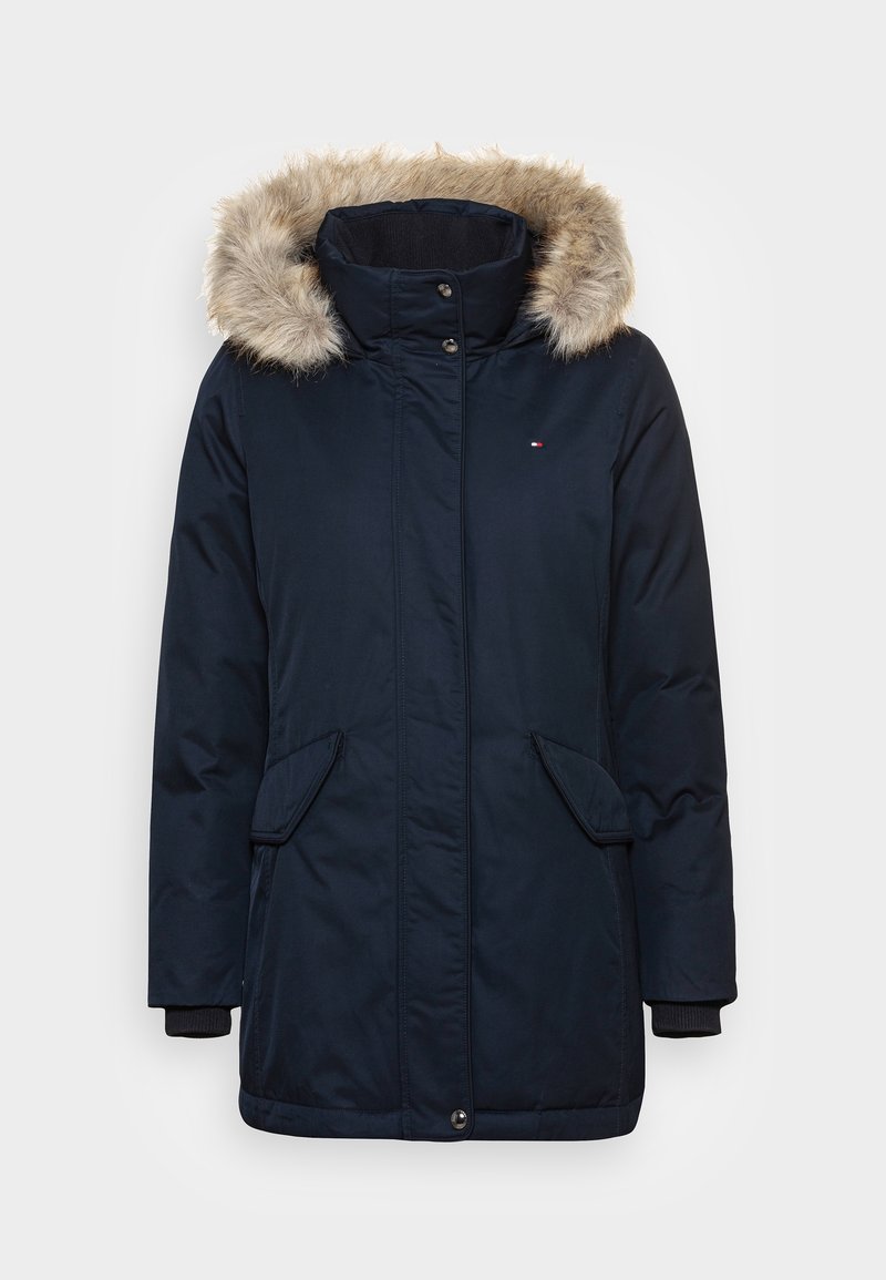 Parka d’hiver bleu marine avec bordure de capuche en fausse fourrure, poches à rabat à l’avant, col montant et fermeture par boutons cachés.