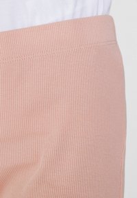 Rosa gerippte Hosen mit einem breiten elastischen Bund und einer glatten Textur, die vertikale Linien auf dem Stoff aufweisen.