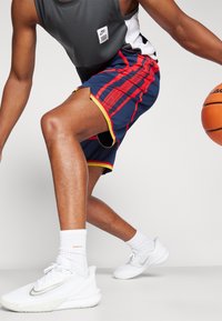 Basketball shorts i navy med røde striber, gule detaljer og sidelæg. Styling med hvide sneakers og ribbede sokker.