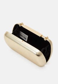 Clutch metálica dorada con una textura suave, forma redondeada y forro interior negro. Presenta un cierre de broche y una marca discreta.