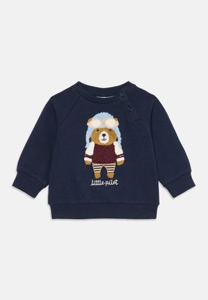 Sweat-shirt marine pour tout-petit avec un ours en peluche portant un casque de pilote et des lunettes, un pantalon rayé, et le texte "petit pilote" sur le devant.