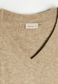 Beżowy sweter w serek wykonany z teksturowanego materiału dzianinowego. Posiada prążkowane wykończenia oraz metkę wewnątrz z nazwą marki i rozmiarem.