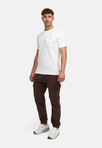 Camiseta blanca de manga corta con un bolsillo en el pecho, combinada con pantalones cargo marrones y zapatillas blancas. Diseñada para la comodidad y la funcionalidad.