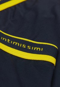Marinblått tyg med en mjuk textur har en gul elastisk midjeband. Midjebandet visar varumärket "intimissimi" i svarta bokstäver.