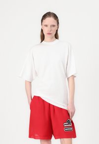 Wit oversized t-shirt met korte mouwen, gecombineerd met rode shorts met een patchdetail. Soepele stof, casual pasvorm en levendige kleuren.