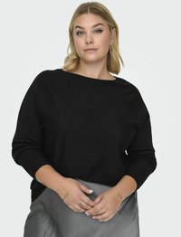 Melna adīta džemperis ar plašu kakla izgriezumu un garām piedurknēm, uzvilkts virs gaiši pelēka satīna svārka. Mīksta tekstūra, vaļīga piegriezuma un nav redzamu rakstu.