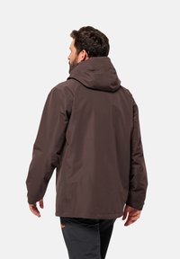 Giacca impermeabile marrone con cappuccio, caratterizzata da una texture liscia e una vestibilità comoda. Dettagli visibili nelle cuciture e nel design sul retro.