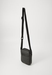 Sac bandoulière noir en simili cuir texturé, avec un compartiment zippé et une bandoulière réglable arborant le logo de la marque.