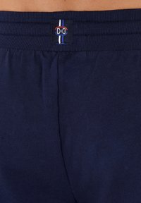 Pantalones cortos de algodón azul marino con una cintura acanalada que presenta un parche con logo y franjas de colores. La tela tiene una textura suave.