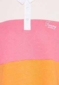 Polo à blocs de couleurs avec col blanc, parties roses et jaunes, boutons blancs et logo Tommy Jeans sur la poitrine.