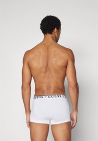 Weiße Baumwoll-Boxershorts mit einem schwarz-roten Markenbund, taillierte Passform und ohne sichtbare Muster, von hinten betrachtet.