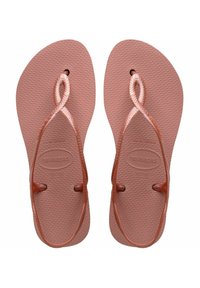 Tongs en caoutchouc marron avec des semelles texturées, dotées de brides tressées qui s'entrelacent au centre et d'un logo intégré sur la semelle.