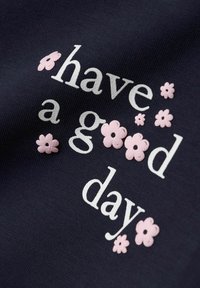 Granatowa tkanina z napisem "miłego dnia" na białym tle, ozdobiona różowymi, haftowanymi kwiatami wokół słów.