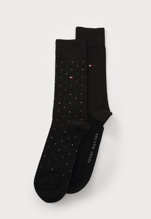 Schwarze Socken mit einem strukturierten Muster, eine mit mehrfarbigen Punkten und die andere unifarben, mit dem Aufdruck "Tommy Hilfiger".