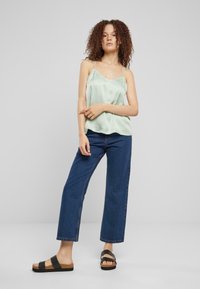 Top de satén verde claro con tirantes finos, combinado con unos vaqueros de pierna ancha en azul y sandalias negras de dedo. Diseño sencillo y corte relajado.