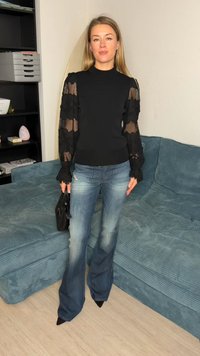 Black long-sleeve top with sheer lace accents and flared sleeves, paired with light blue flared jeans and black pointed shoes, with a black handbag.