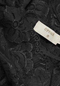 Zwart kant met bloemmotieven, complexe texturen en een zichtbaar crèmekleurig label met de merknaam.