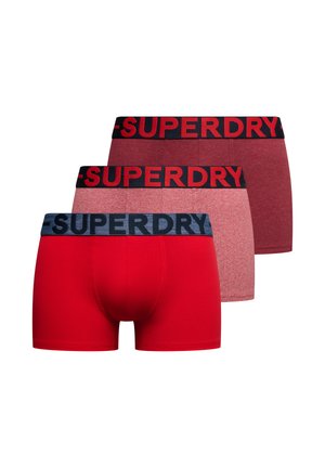 Trzy pary męskich bokserek w czerwieni i odcieniach bordowego, każda z markowanym elastycznym pasem z napisem „SUPERDRY”.