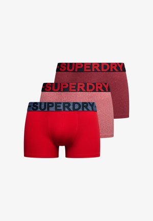 Tre par herre boxershorts i rød og nuancer af mørkerød, hver med et elastisk bånd med mærket "SUPERDRY".