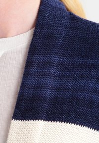 Närbild av en person som bär ett marinblått och krämfärgat randigt tyg, som visar en del av en vit topp under och hud nära kragen.