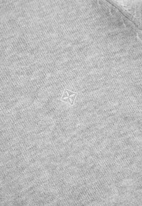 Szara dzianina prezentująca subtelny, fakturowany wzór z wyhaftowanym w centrum kwadratowym logo, przedstawiającym prosty geometryczny design.