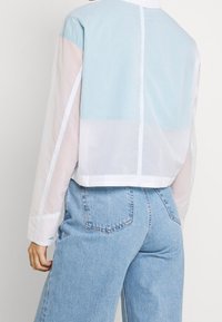 Giacca corta a blocchi di colore con pannelli azzurri, rosa e bianchi. Presenta una texture liscia e semi-trasparente e un colletto classico.