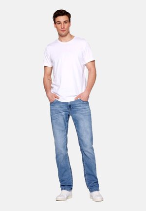Camiseta de algodón blanca, jeans de mezclilla azul y zapatillas blancas. Los jeans tienen un ligero desgaste, con costuras visibles a lo largo de las costuras.
