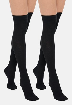 Δύο ζεύγη ποδιών με μαύρες ριγωτές κάλτσες πάνω από το γόνατο σε απλό γκρι φόντο.