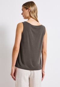 Top grigio senza maniche con scollo rotondo, texture del tessuto liscia e dettagli di cucitura sottili, abbinato a pantaloni di colore chiaro.