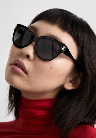 Schwarze Cat-Eye-Sonnenbrillen mit dunklen Gläsern, glänzendem Rahmen und goldfarbener Hardware an den Schläfen, die ein elegantes, modernes Design aufweisen.