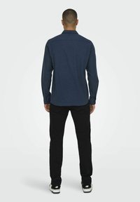 Marineblå knap-op skjorte med lange ærmer og krave, lavet af et struktureret stof, parret med sorte jeans og sorte sneakers.