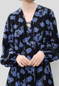 Černé šaty s modrým květinovým vzorem, hlubokým V výstřihem s šněrováním a dlouhými vypufovanými rukávy se staženými manžetami, hladká textilie.