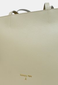Borsa tote in pelle beige con texture liscia, design semplice e logo dorato stampato. Presenta due manici corti e cuciture pulite.