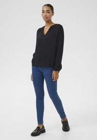 Black long-sleeve blouse with a V-neck and gathered cuffs, paired with blue skinny jeans and black loafers. Smooth texture, simple design.