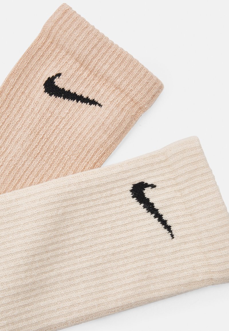 Para prążkowanych skarpet w jasnym beżu i kremie, z czarnymi logo Nike swoosh na każdej skarpecie. Miękka faktura z dopasowanym krojem.
