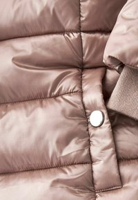 Chaqueta acolchada rosa con tejido brillante, con paneles cosidos, un botón a presión plateado y un detalle de puños de punto acanalado.