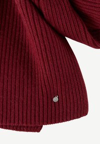 Tessuto a maglia rosso a coste con una texture morbida, caratterizzato da un piccolo tag in argento vicino all'orlo.